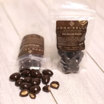 Two bag of dark chocolate covered almonds. One is standing and the other is laying down with the chocolate covered nuts spilled out.
