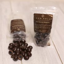 Two bags of dark chocolate covered blueberries. One sits upright while the other is laying down, mostly spilled out onto the table.