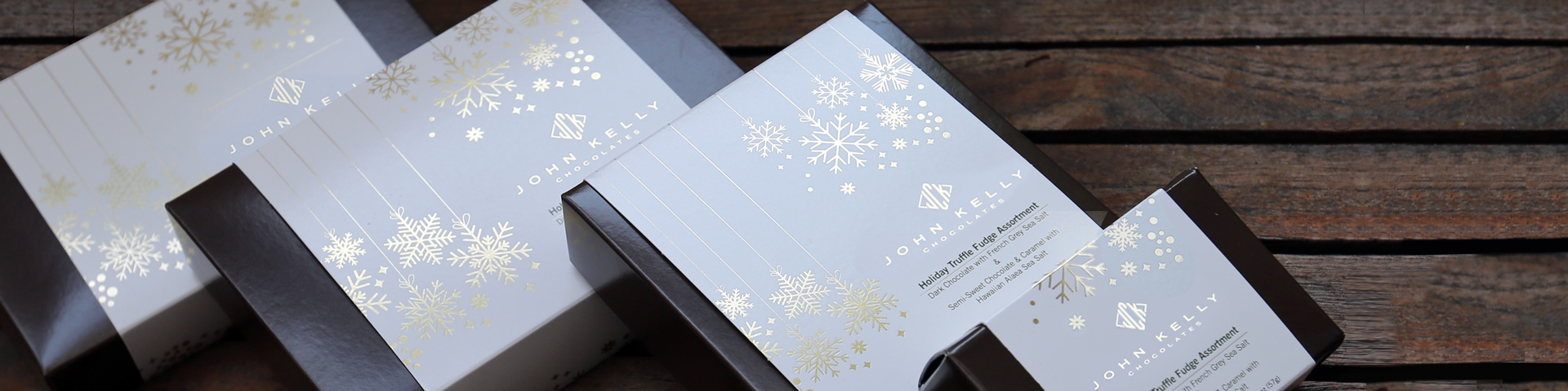 Four holiday boxes leaning against each other. Each box has a white sleeve with gold snowflakes on it.