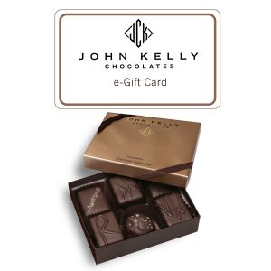 A box with a John Kelly Chocolates logo on it reads e-Gift Card. Beneath the box is an open six piece assortment. Six chocolates from the assortment show with the lid partially on the box. The lid has a brown ribbon on it.