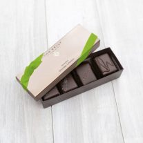 An open 4 piece assortment box with 4 different chocolates from the assortment showing with a lime ribbon on the lid