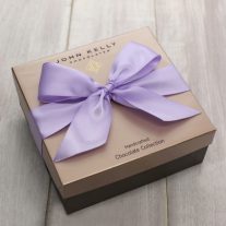 A closed 24 piece assortment box. The lid of the box is gold and is finished with a orchid color ribbon