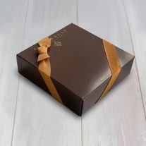 A closed 4 piece assortment box with a gold ribbon. The box is brown and had a gold John Kelly Chocolates logo