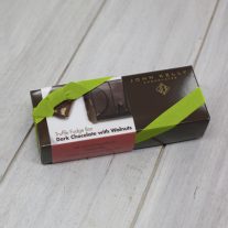 A dark brown rectangular box with a red dark chocolate with walnuts sleeve on it. It is closed with a lime stretchy ribbon.