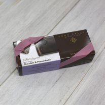 A dark brown rectangular box with a purple semi-sweet peanut butter chocolate sleeve on it. It is closed with an orchid stretchy ribbon.